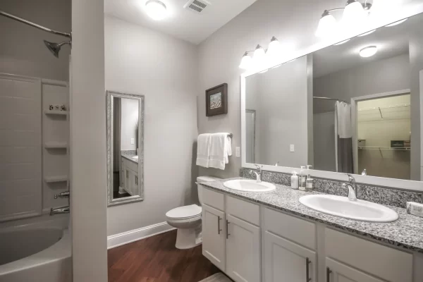 Bathroom with dual vanity sinks with granite countertop, hardwood-style floors, toilet, and shower bath