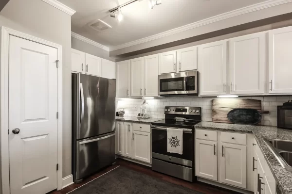 Kitchen with hardwood style flooring, granite countertops, white cabinetry, subway tile backsplash, and stainless steel energy efficient appliances including a refrigerator, microwave, stove, oven, sink, and dishwasher